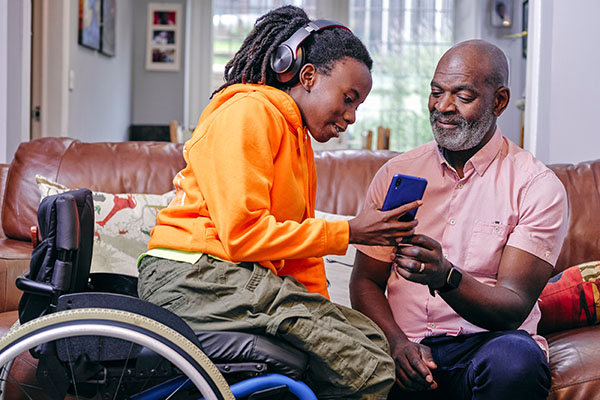 A dad and his daughter in a wheelchair looking at a phone