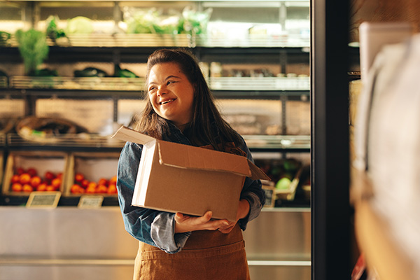 Woman with Down syndrome smiling happily while working as a shopkeeper in a grocery store.