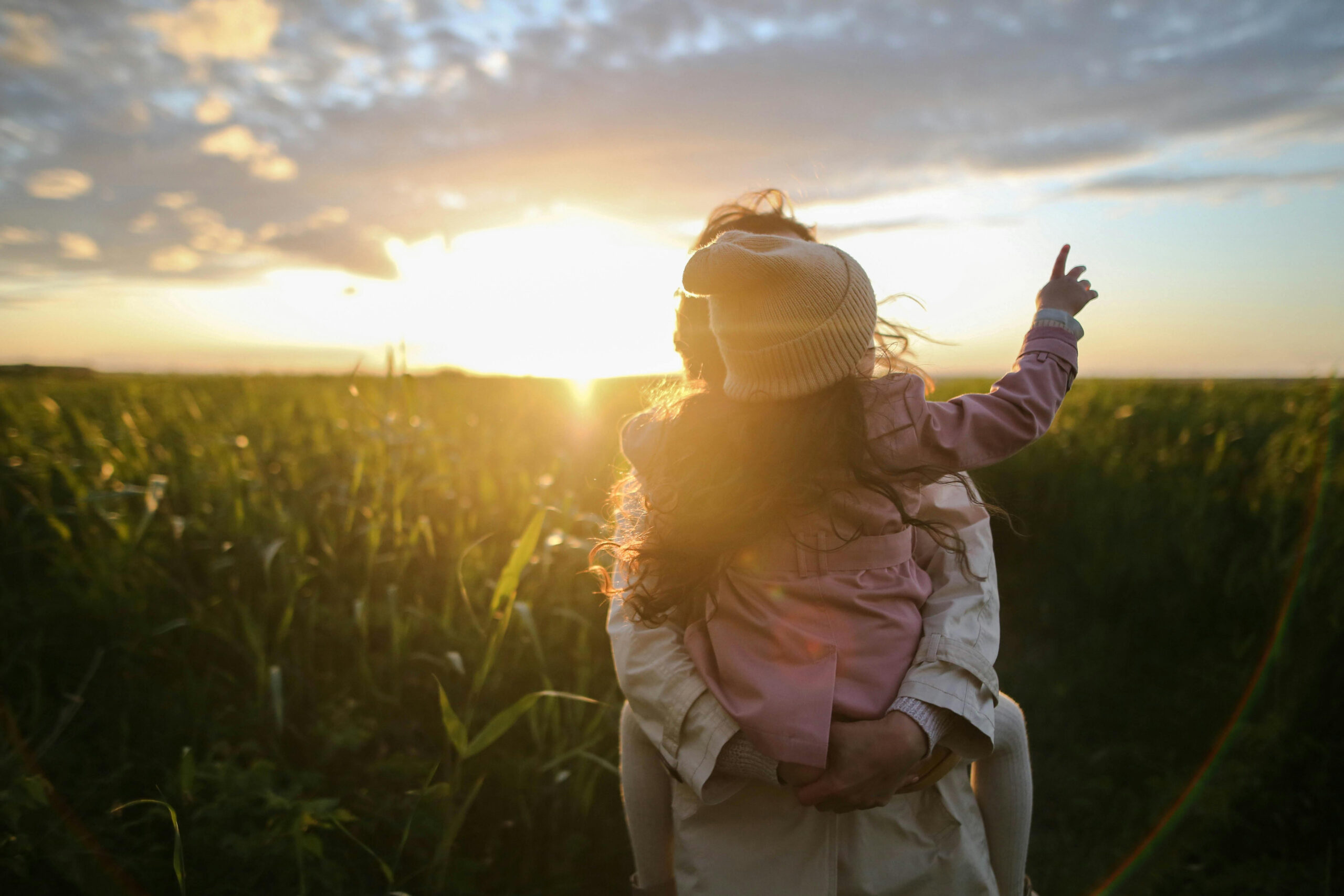 a parent carrying their daughter with the sunset in the background