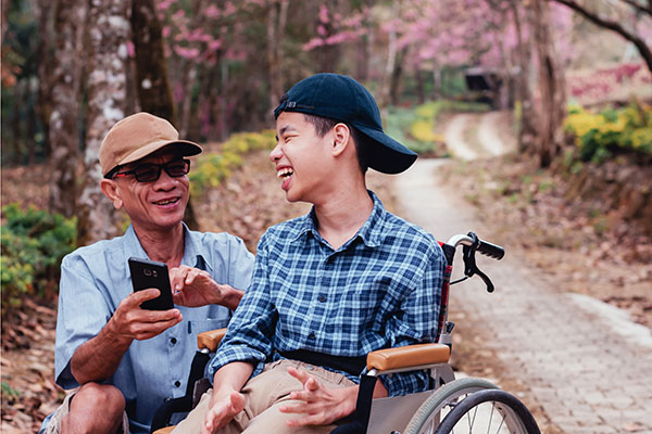 a dad with his son on a wheelchair looking at a phone