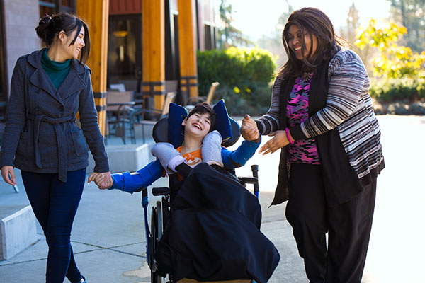 a disabled boy in a wheelchair holding hands with his caregivers