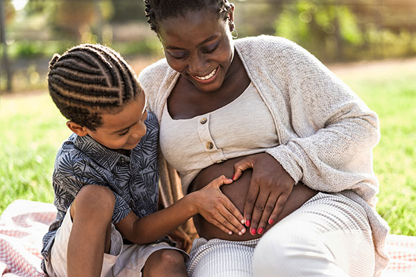 a pregnant mom with her older son making a heart shape with their hands on her pregnant belly