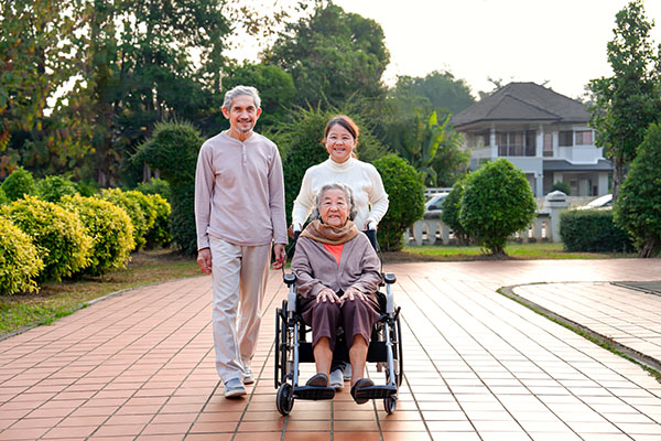 senior grandmother sitting in a wheelchair, smiling, while her daughter and son in law help her