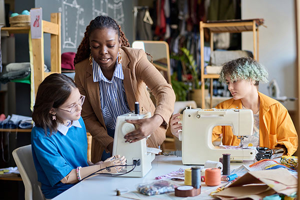 A woman showing two girls with disabilities how to sew