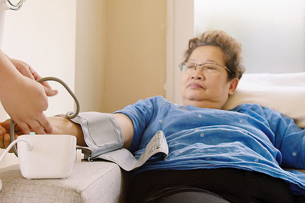 an asian woman on her couch taking her blood pressure